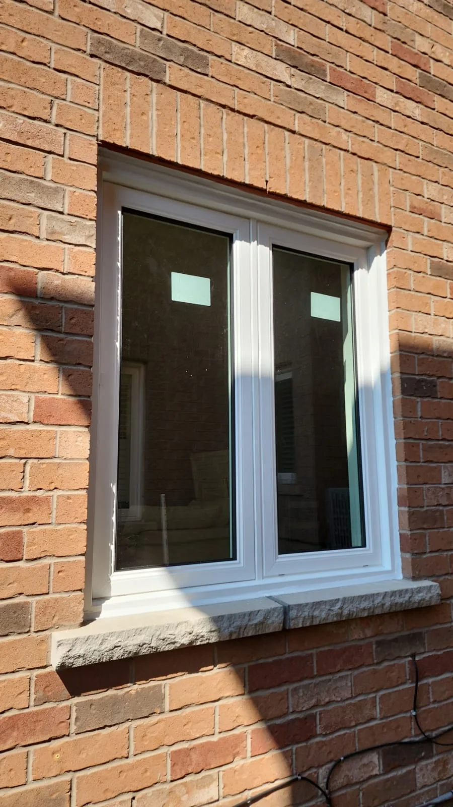 Two-panel white window installed in a red-brick wall above a stone sill