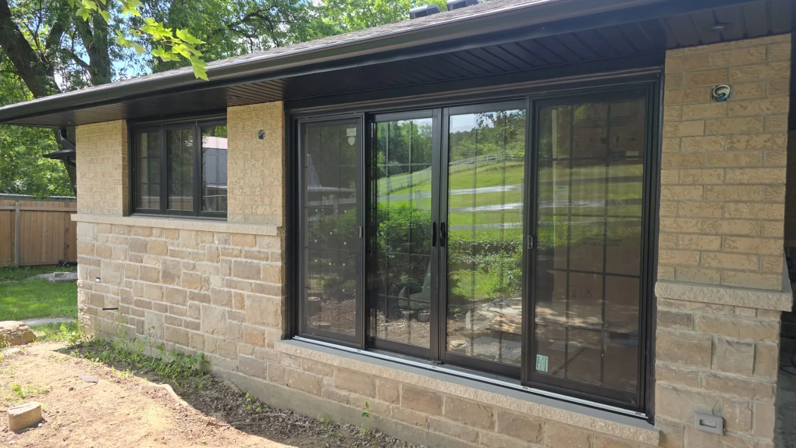 Three-panel black-framed sliding patio door across the back of a stone bungalow