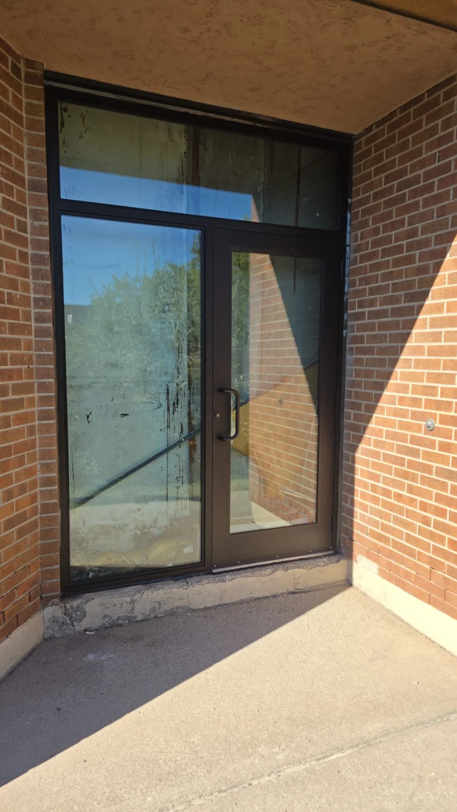 Dark-framed glazed commercial entrance with a transom in a recessed brick opening