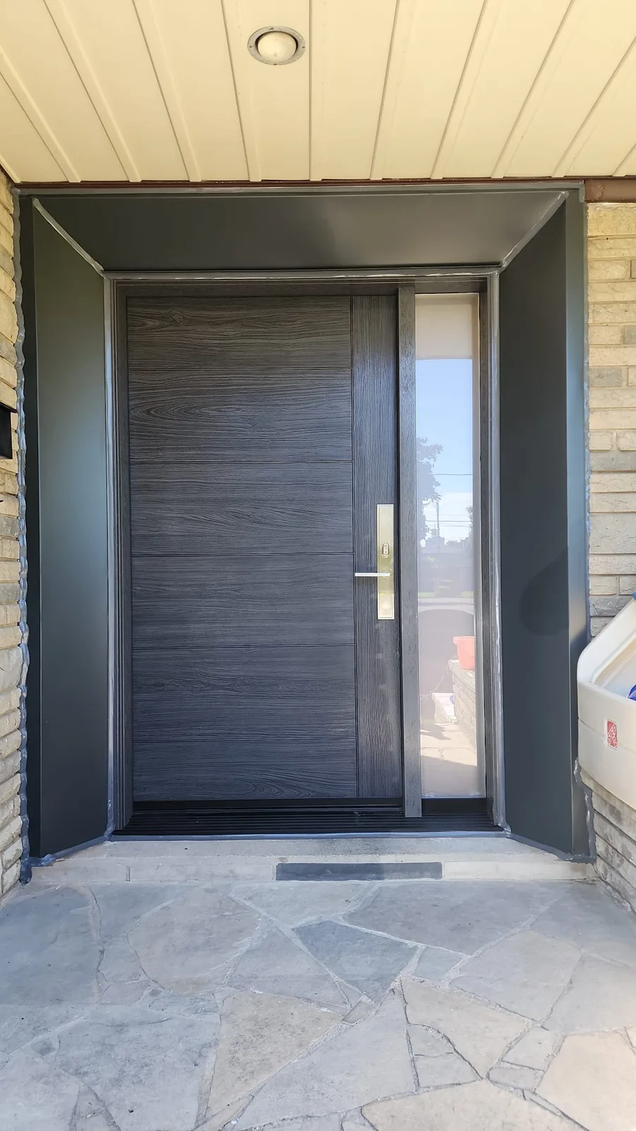 After: Finished dark front door and sidelite framed by dark metal trim on a stone porch