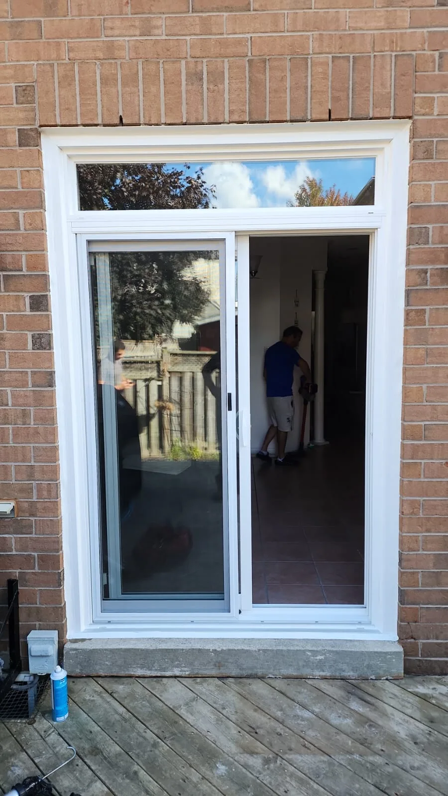 White sliding patio door with a transom window above, set into a brick wall and opening onto a deck