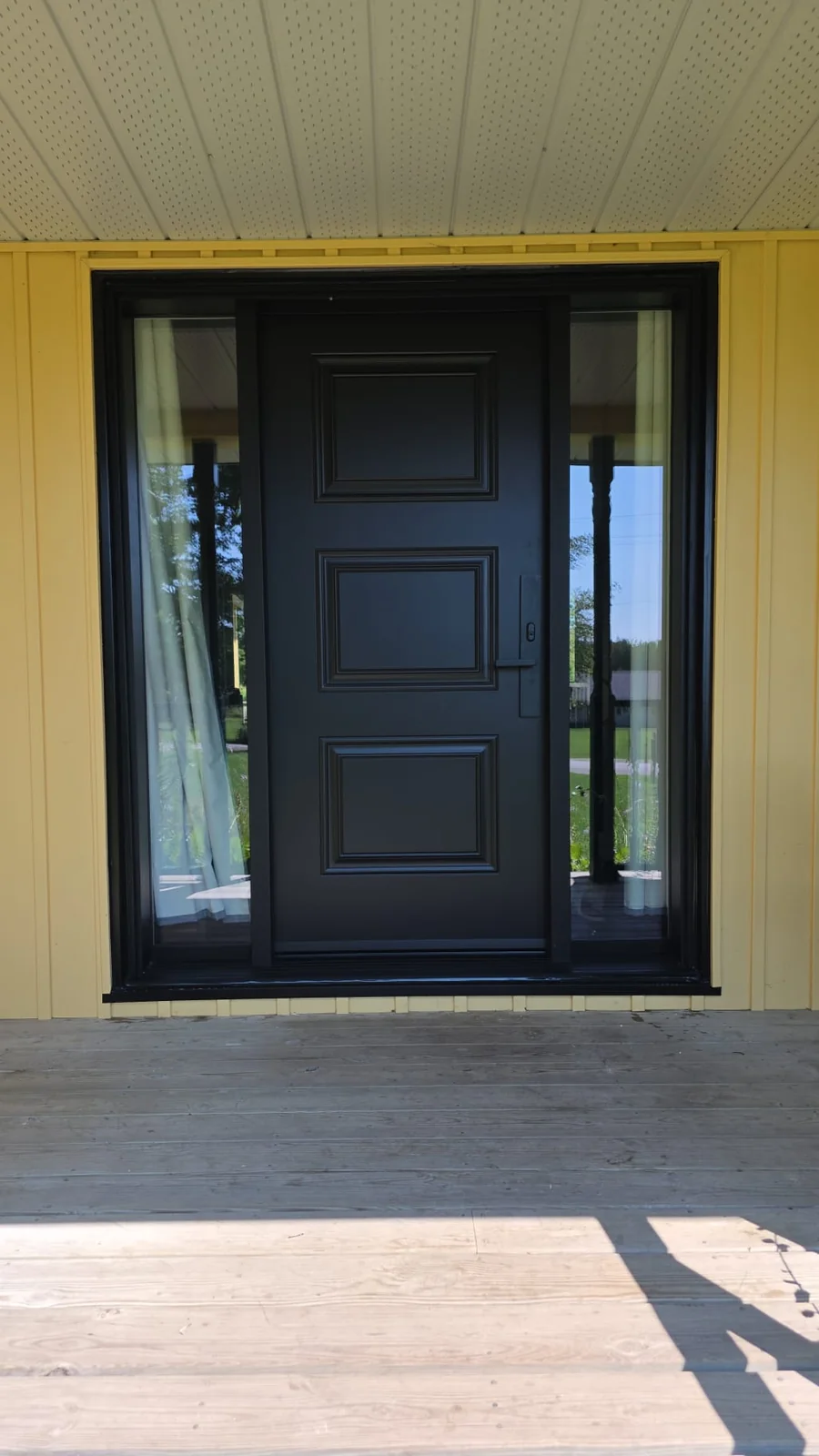 Dark panelled front door with glazed sidelights beneath a covered porch