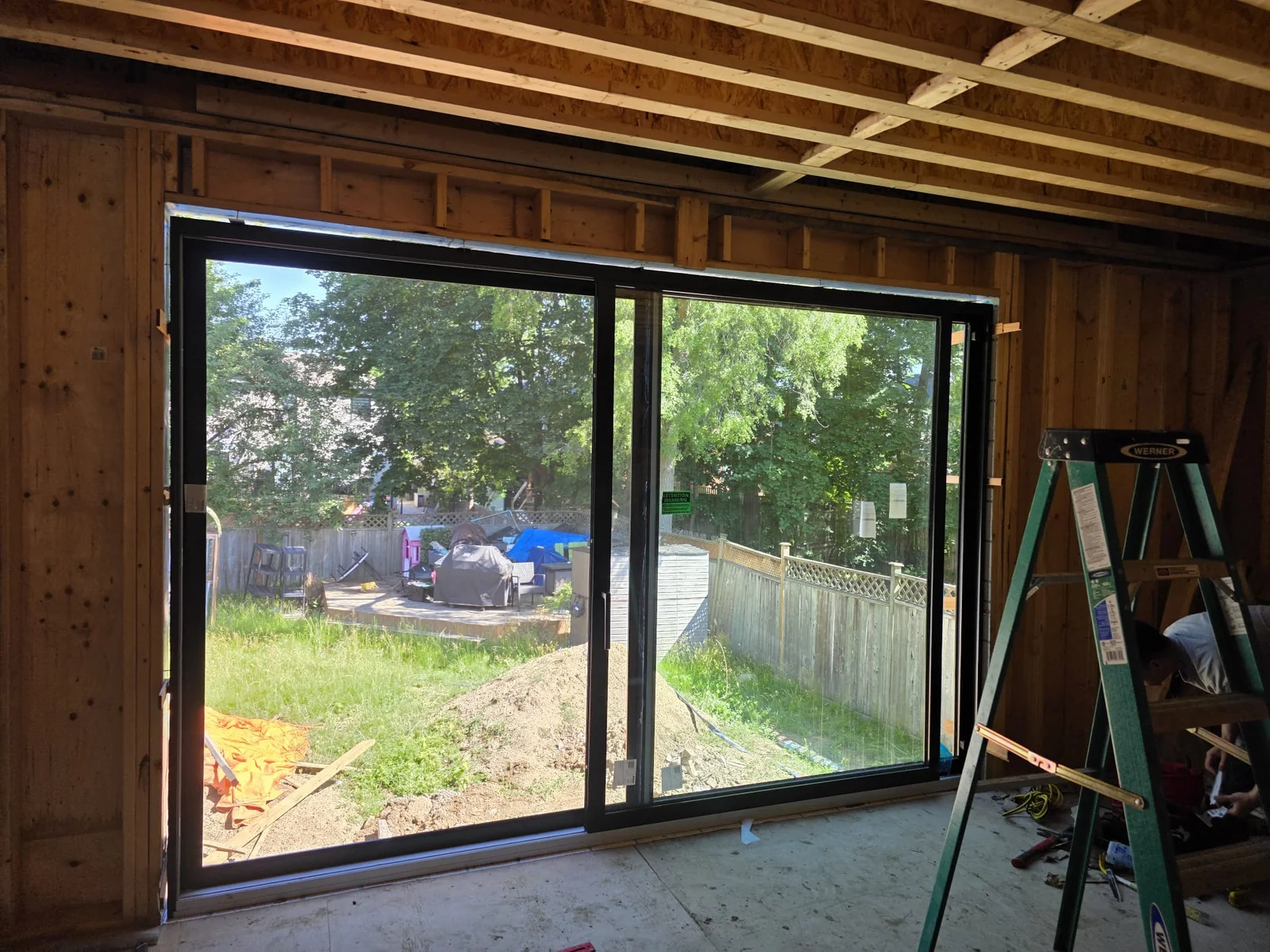 Wide dark-framed sliding patio door inside a timber-framed house under construction
