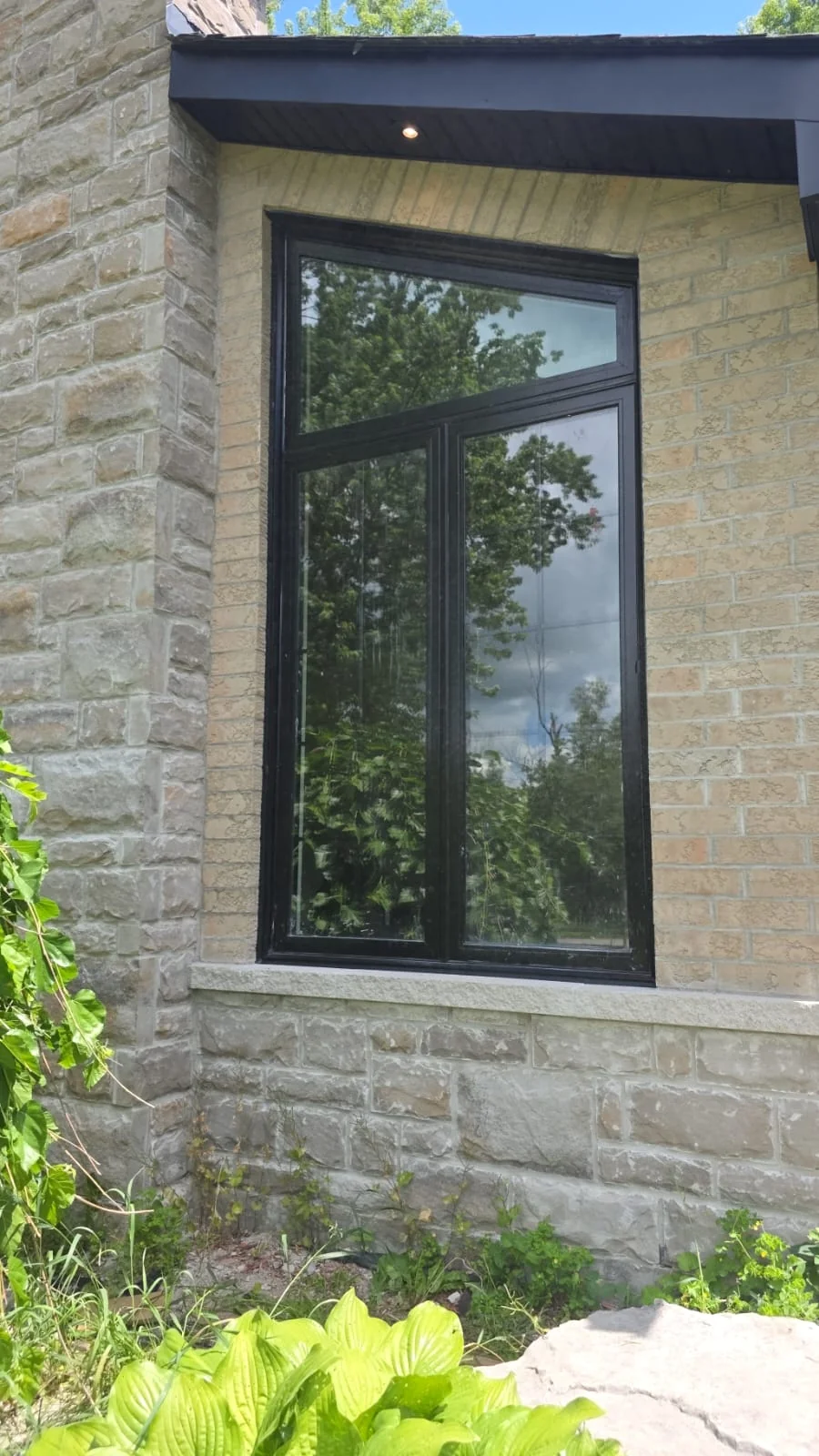Tall dark-framed window set into a stone wall beside a wooded garden